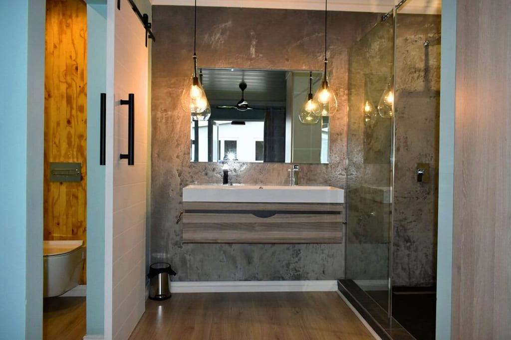 Modernes Badezimmer mit Waschbecken, Spiegel, Hängelampen und Glasdusche, offene Tür zur Toilette