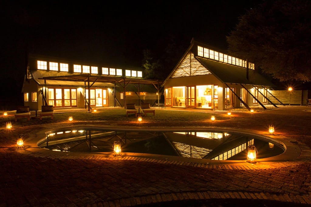 Beleuchtete Lodge mit Laternen und spiegelndem Pool in der Nacht