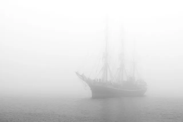 Segelschiff als schwache Silhouette im dichten Nebel über ruhigem Meer