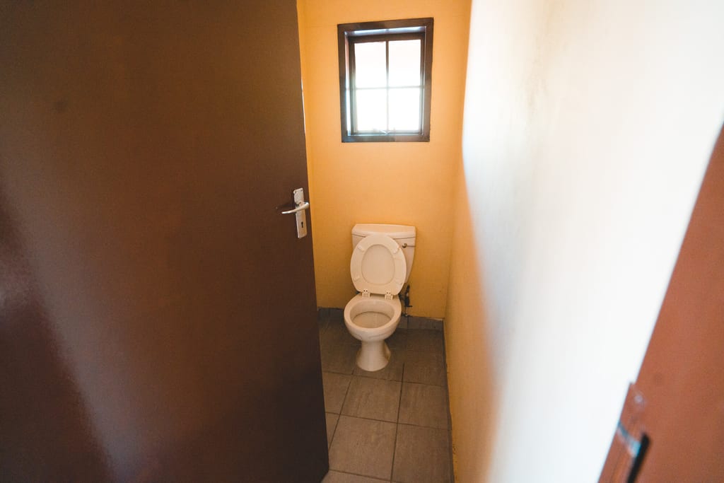 Kleines WC mit offener Tür, Toilette und kleinem Fenster, gesehen aus der Türöffnung.