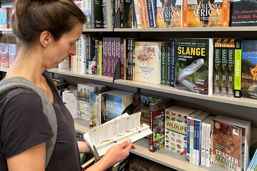 Frau liest konzentriert ein Buch vor einem Regal mit Natur- und Tierbüchern im Buchladen.