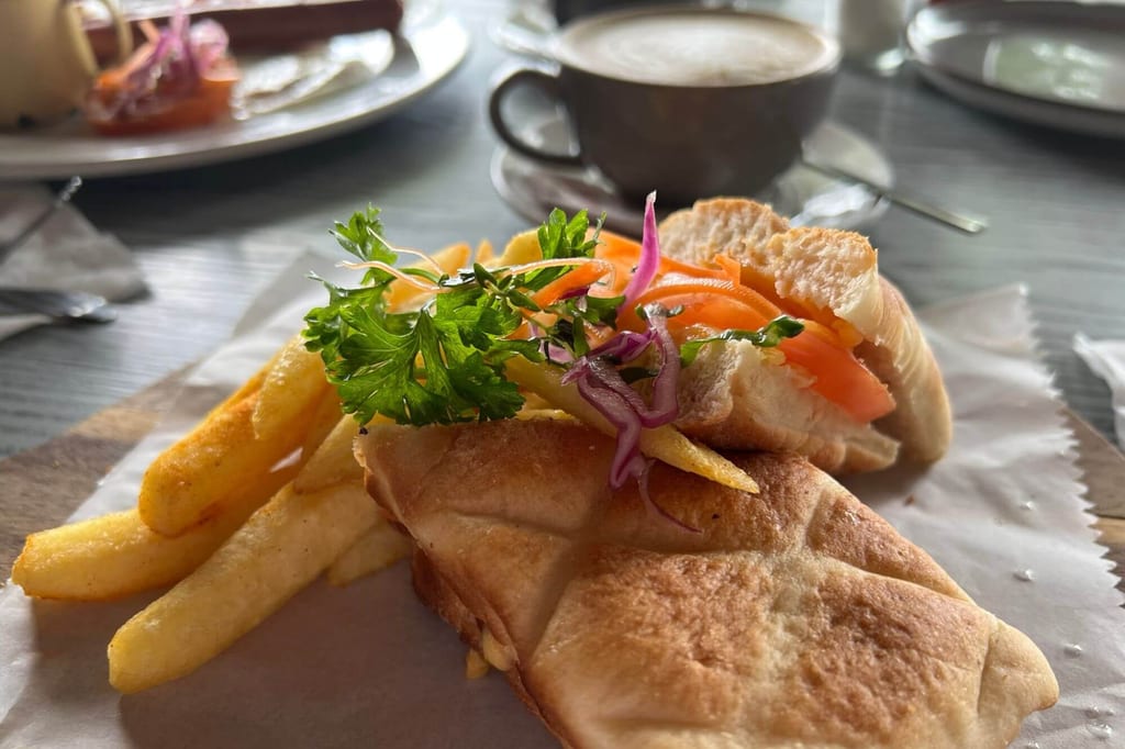 Nahaufnahme eines belegten Sandwichs mit Pommes und einer Tasse Kaffee auf dem Tisch.