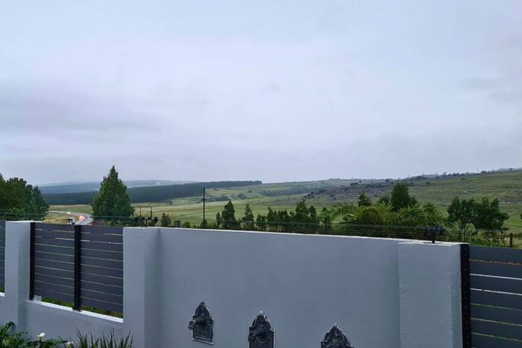 Blick über Mauer und Zaun auf hügelige grüne Landschaft unter bewölktem Himmel
