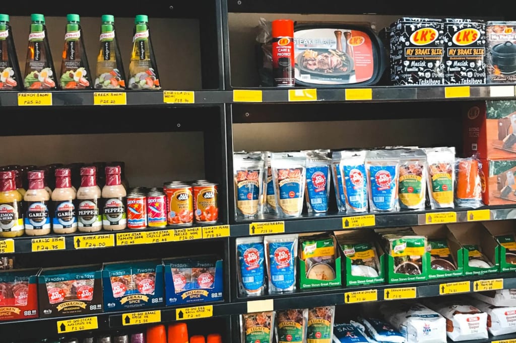 Supermarktregal mit verschiedenen Gewürzen, Soßen und Snacks in Verpackungen und Preisschildern.