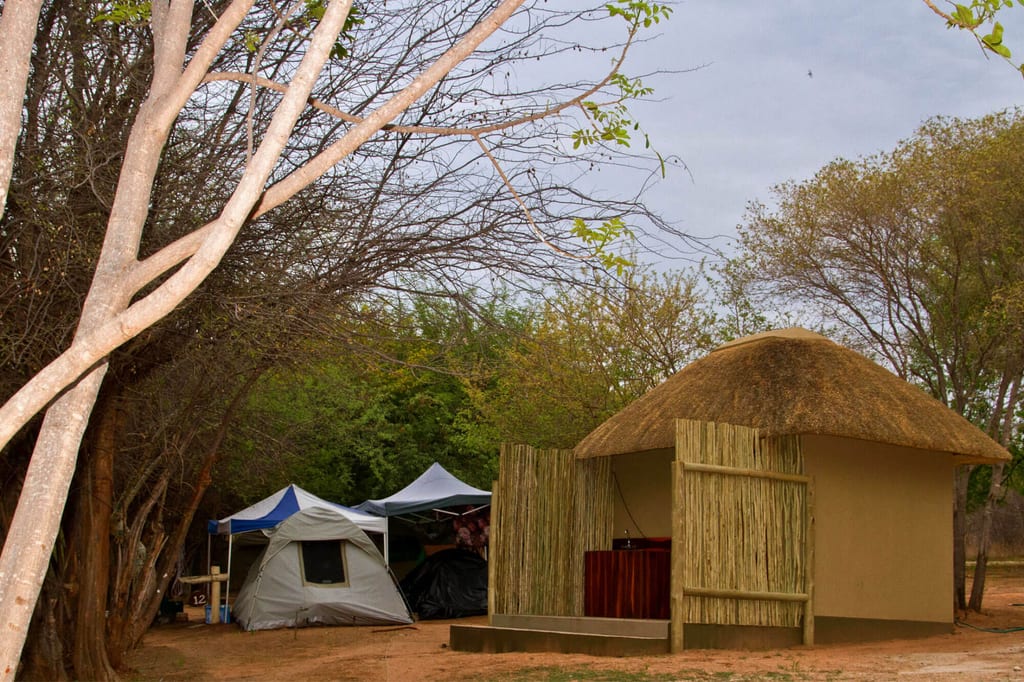 Zeltcamp neben einer kleinen Hütte mit Strohdach unter kahlen Bäumen.
