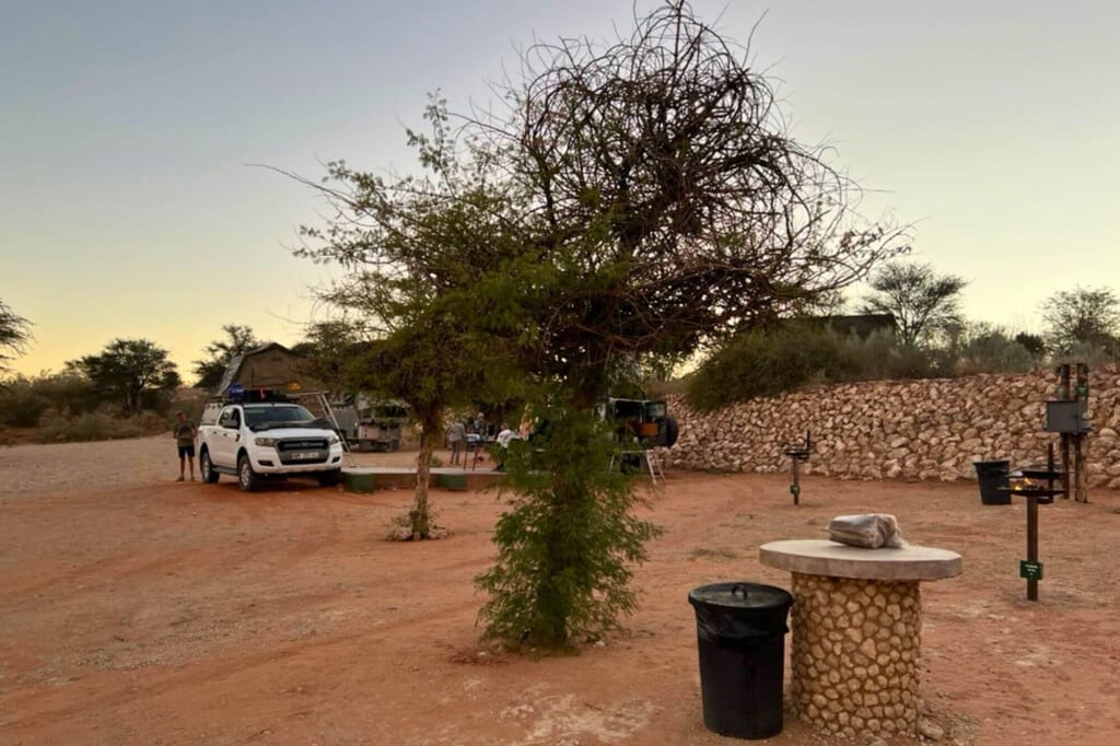 Freier Campingplatz mit Geländewagen, Zelt, Baum und Steinmauer bei Abenddämmerung.