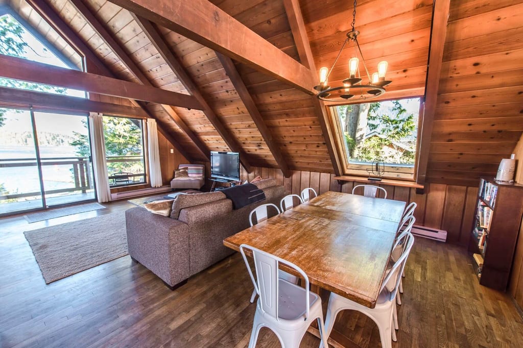 Gemütliches Holzloft mit Esstisch, Sofa und großem Fenster zum See