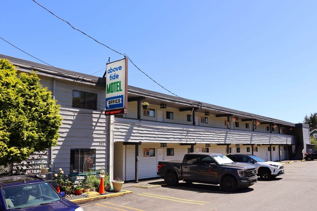 Zweistöckiges Motel mit Parkplätzen, Schild ‚above tide MOTEL OFFICE‘ und blauer Himmel