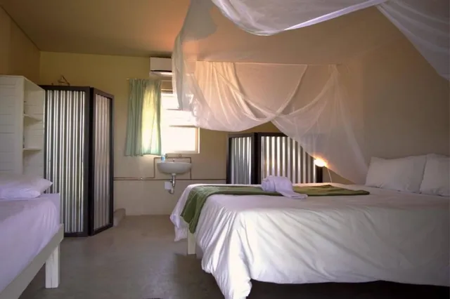 Schlichtes Gästezimmer mit Moskitonetz, zwei Betten und Waschbecken bei sanftem Tageslicht.