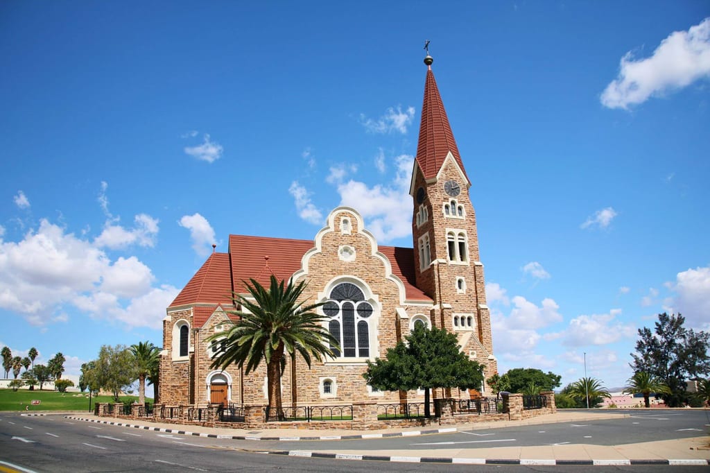 Vorderansicht einer Steinkirche mit hohem Turm, roten Dächern und Palmen in Windhoek, Namibia.