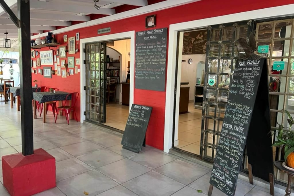 Überdachte Café-Terrasse mit roter Wand, Speisekarten auf Tafeln und roten Stühlen.