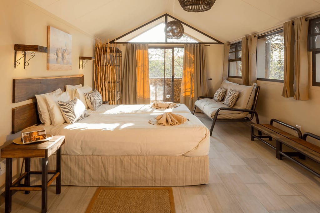 Helles Safari-inspiriertes Zimmer mit zwei zusammengeschobenen Betten, Zebra-Kissen und Terrasse im warmen Morgenlicht.
