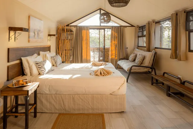 Helles Safari-inspiriertes Zimmer mit zwei zusammengeschobenen Betten, Zebra-Kissen und Terrasse im warmen Morgenlicht.