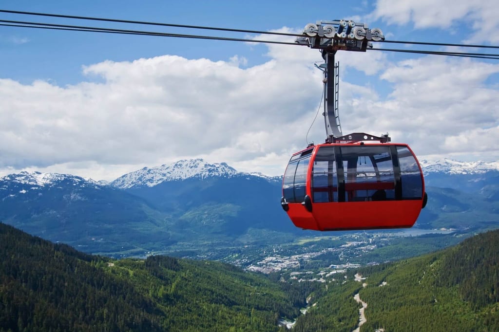 Rote Gondel einer Seilbahn vor schneebedeckten Bergen und grünem Tal bei bewölktem Himmel.