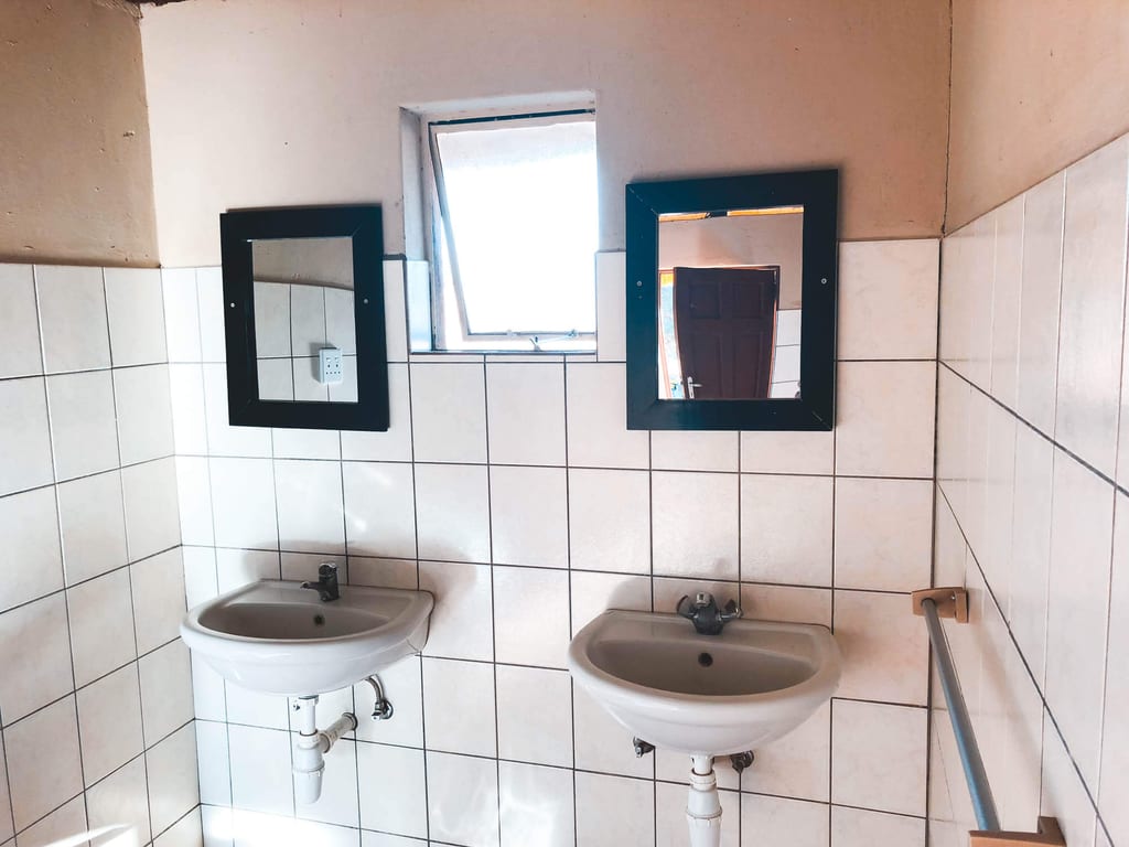 Zweifaches Waschbecken mit zwei Spiegeln und Kacheln, Tageslicht durch kleines Fenster.