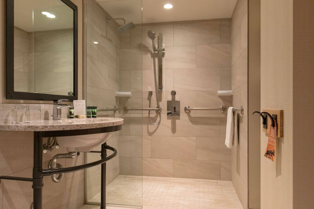 Modernes Badezimmer mit ebenerdiger Dusche, Haltegriffen und Waschbecken in warmem Licht.