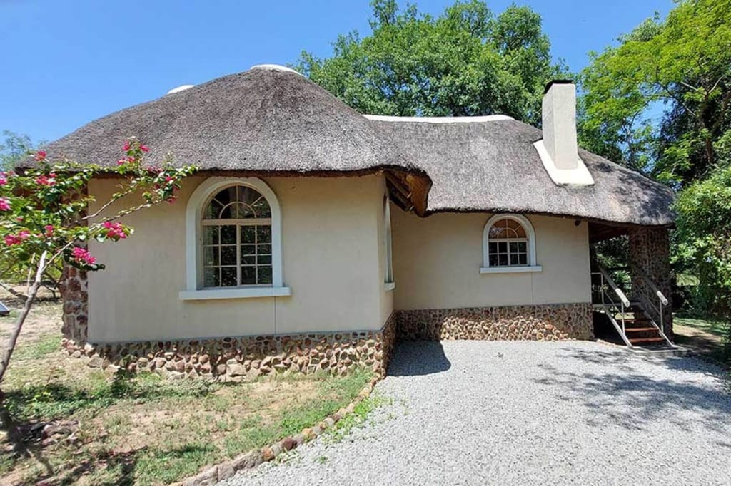 Strohgedecktes Landhaus mit Rundbogenfenstern, Kiesplatz und Bäumen bei klarem Tageslicht