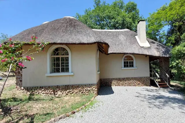 Strohgedecktes Landhaus mit Rundbogenfenstern, Kiesplatz und Bäumen bei klarem Tageslicht