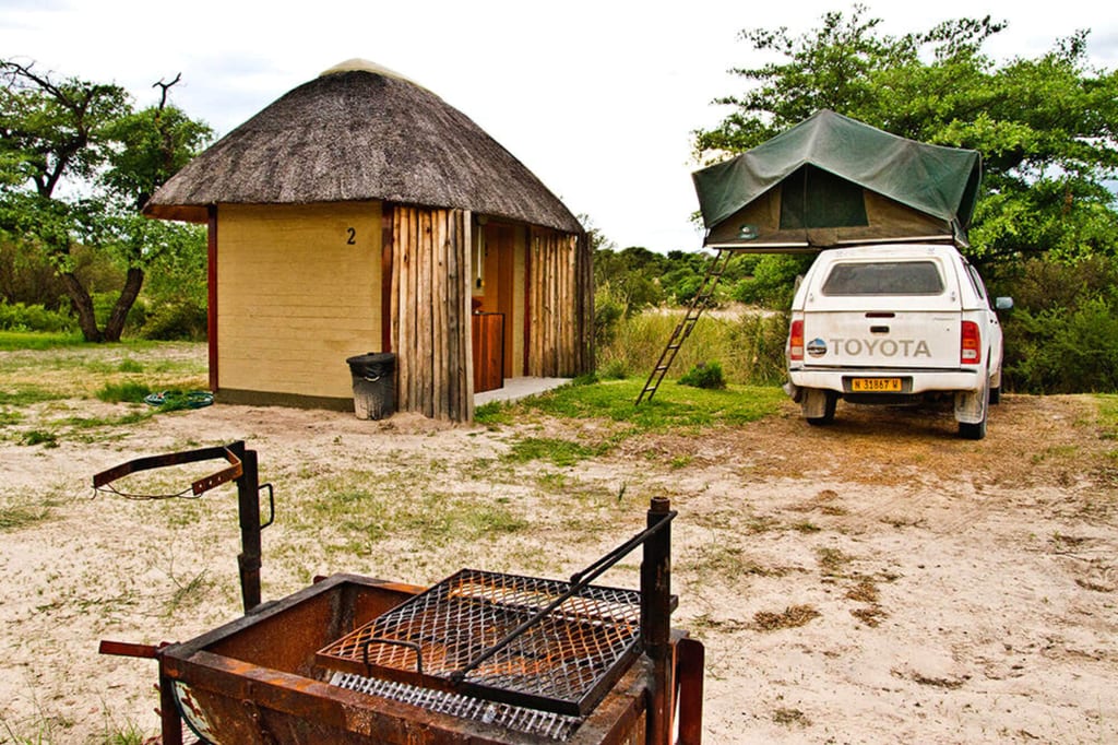 Campingplatz mit strohgedecktem Häuschen, Toyota-Pickup mit Dachzelt und Grill im Vordergrund