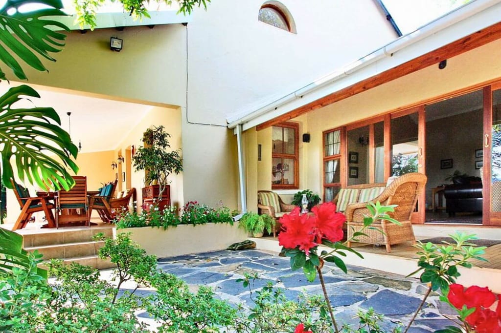 Gartenblick auf helle Veranda mit Korbmöbeln, Essbereich und roten Blumen im Vordergrund