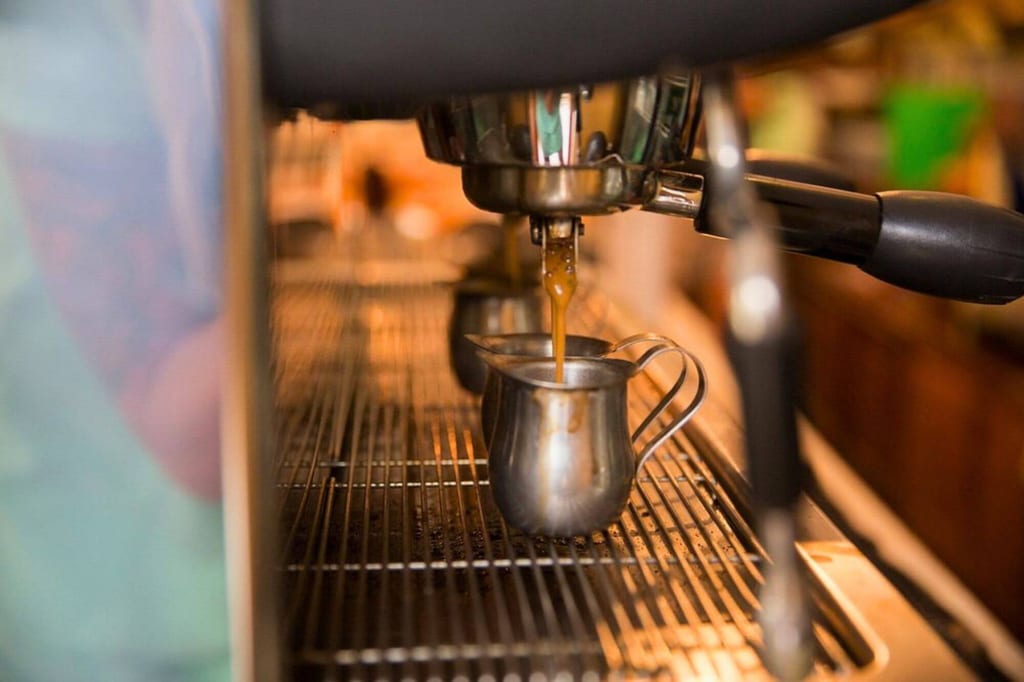 Nahaufnahme: Espresso fließt aus einer Siebträgermaschine in eine kleine Metallkanne.