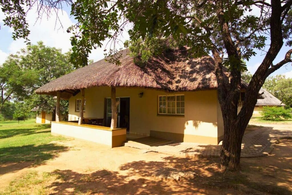 Strohgedeckter Bungalow mit Veranda unter Bäumen bei sonnigem Tageslicht