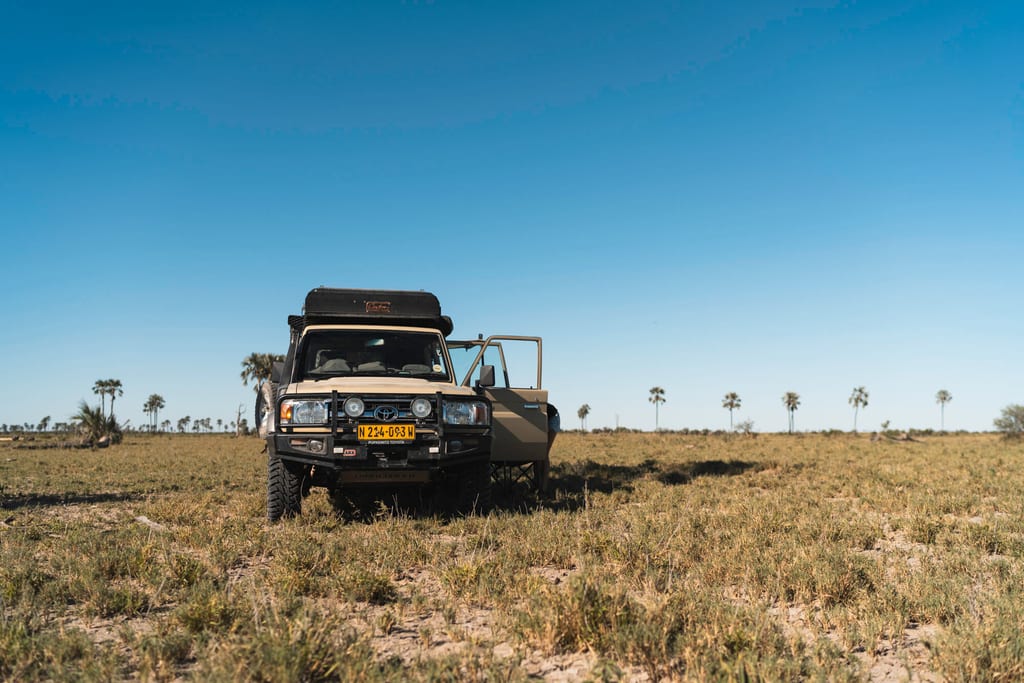 Geländewagen auf weiter, trockener Grassteppe unter klarem blauem Himmel, Frontalansicht mit offener Tür.