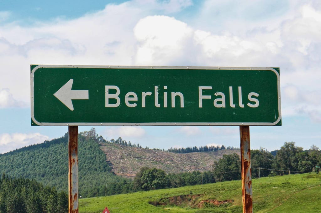 Grünes Wegweiser-Schild mit Aufschrift "Berlin Falls" vor hügeliger, teils gerodeter Waldlandschaft