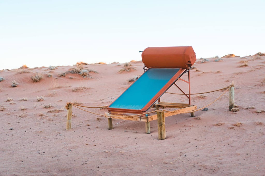Solardusche auf Holzgestell in sandiger Dünenlandschaft bei warmem Licht