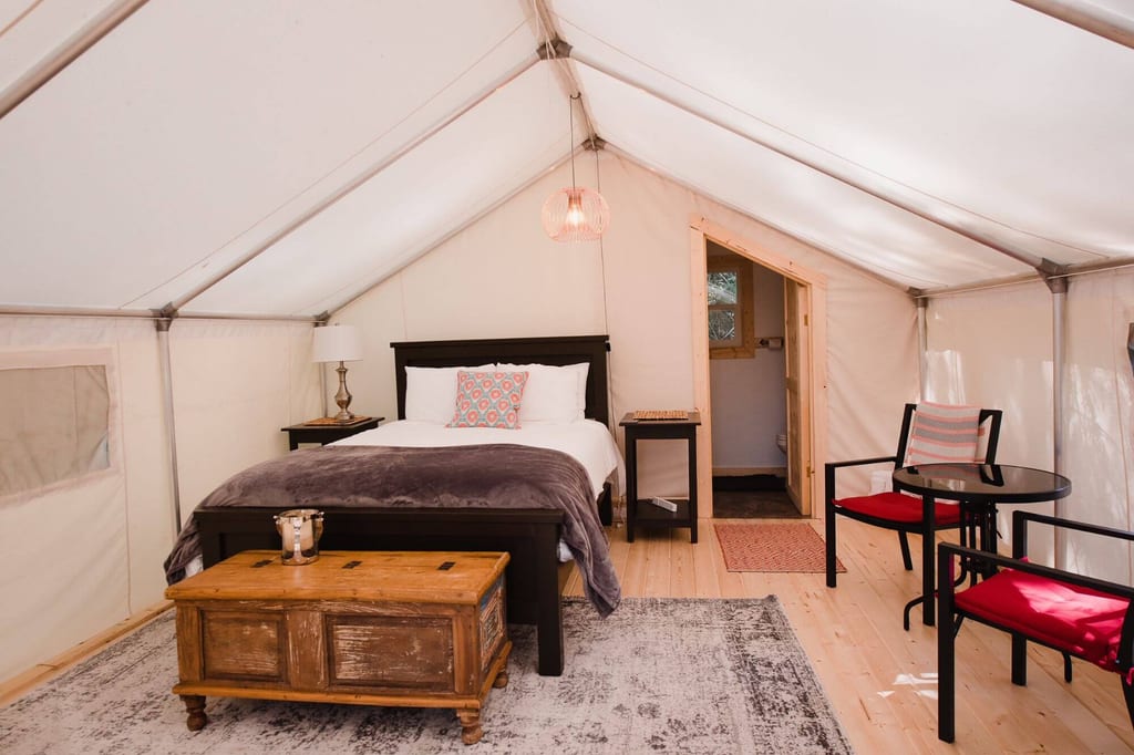 Innenansicht eines gemütlichen Glamping-Zelts mit Bett, Holztruhe und Sitzbereich.