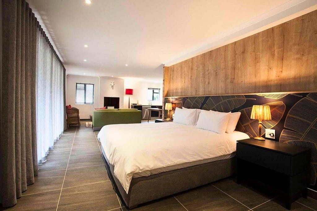 Modernes Schlafzimmer mit großem Bett, Holz-Akzentwand und Sitzbereich, warmes Licht