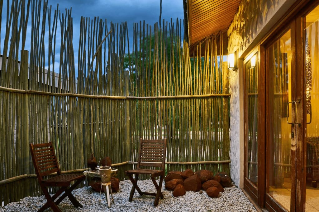 Gemütliche Patio mit Holzsichtschutz, zwei Stühlen und warmer Beleuchtung bei Dämmerung.