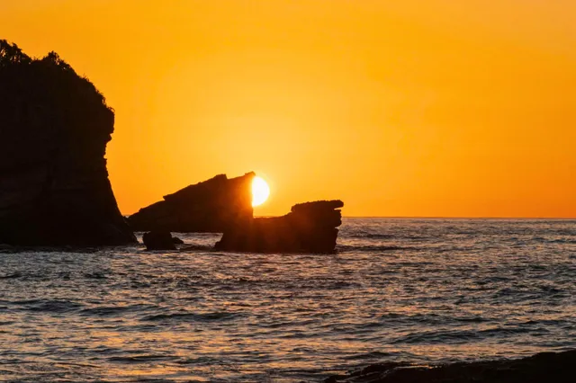 Sonnenuntergang hinter Felsformation im Meer bei Samara, Costa Rica, orange Silhouette