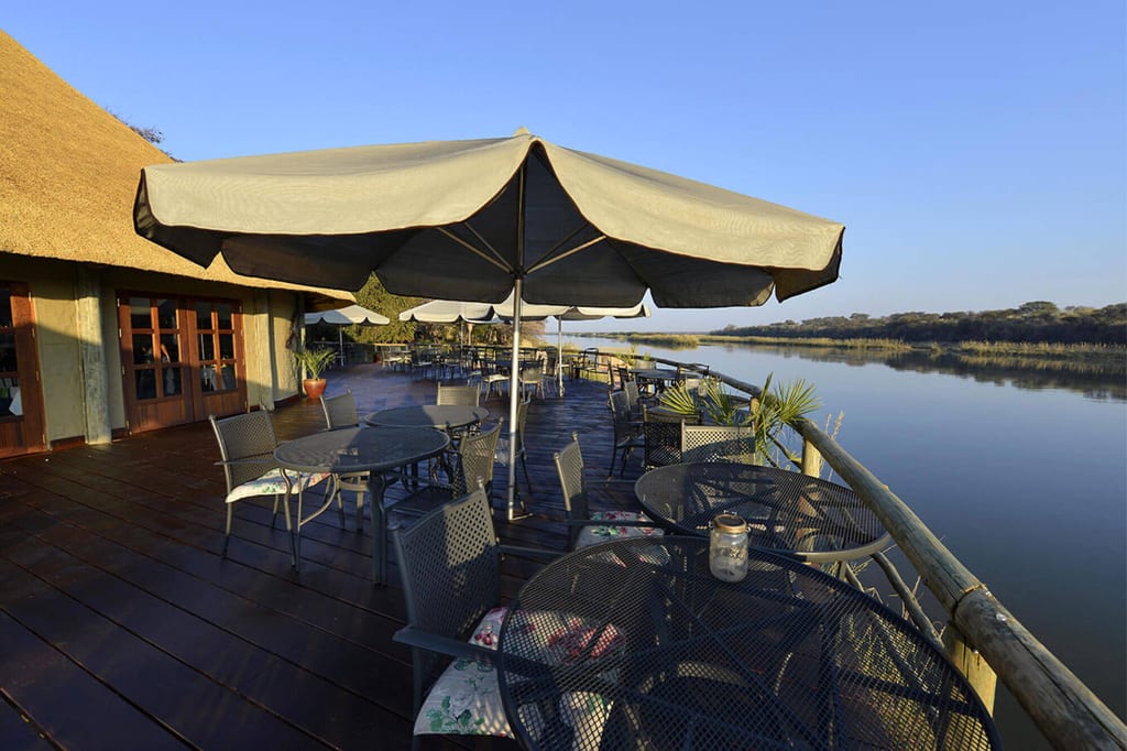 Terrasse mit Tischen und Sonnenschirmen am ruhigen Flussufer bei klarem Himmel