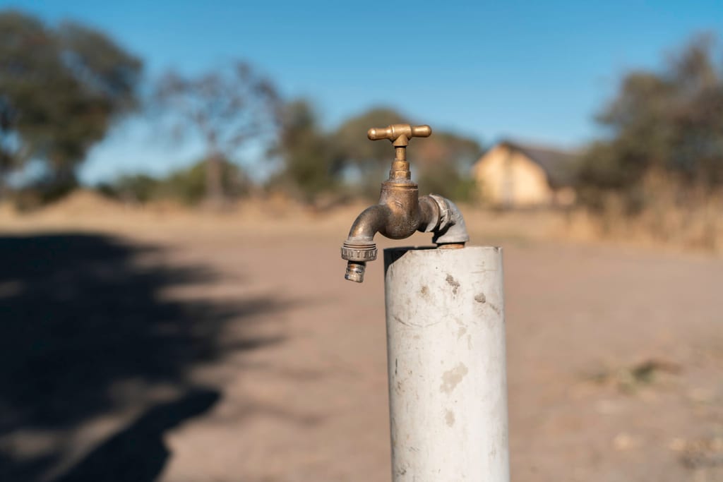 Nahaufnahme eines Metall-Wasserhahns auf einem Rohr vor trockener, sonniger Landschaft