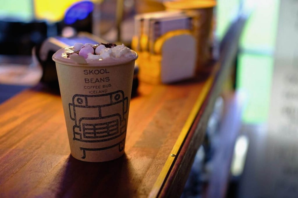Papierbecher mit Marshmallows und Sahne auf hölzerner Cafétheke, warmes Licht und unscharfer Hintergrund.