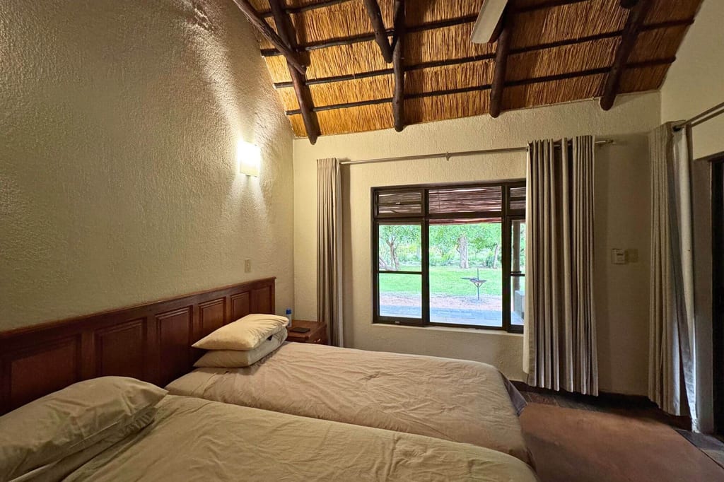 Gemütliches Schlafzimmer mit zwei Einzelbetten, Schilfdach und Fenster zum grünen Außenbereich.