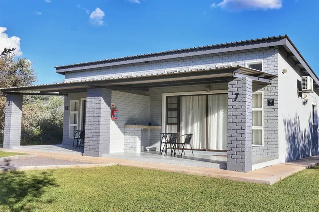 Ferienhaus mit überdachter Veranda, zwei Stühlen und gepflegtem Rasen bei sonnigem Himmel
