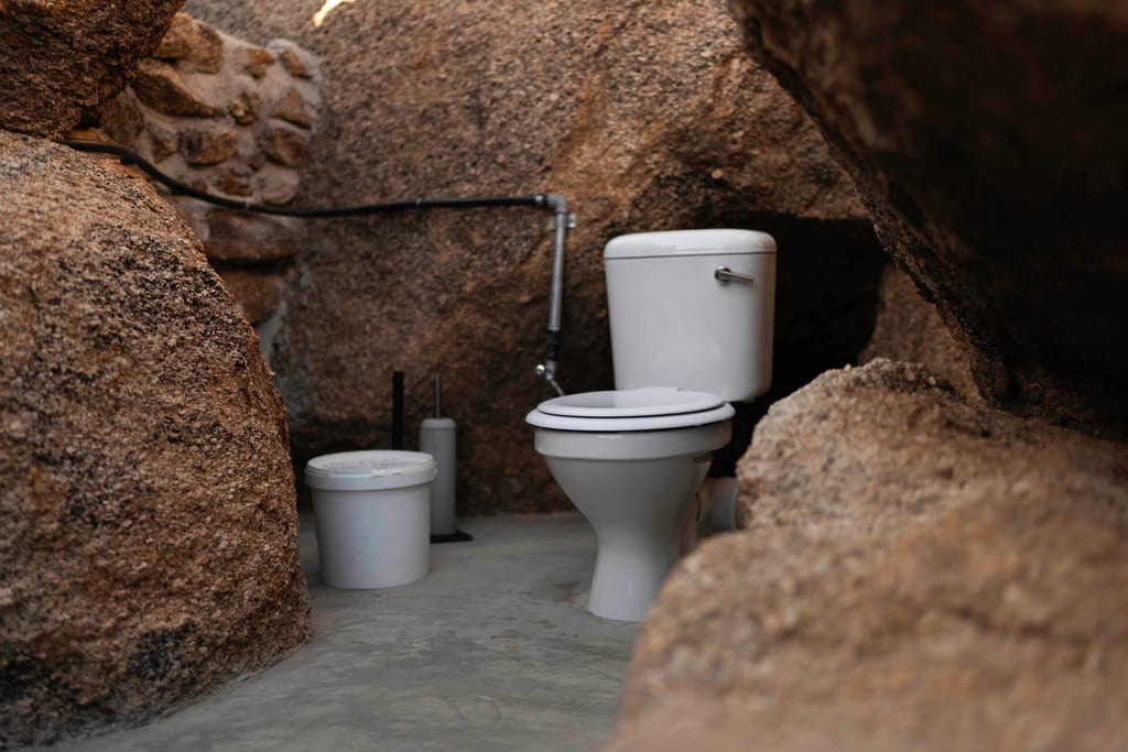 Freistehende Toilette zwischen rauen Felsen in einer provisorischen Außenanlage.