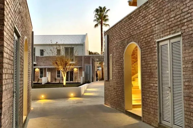 Innenhof mit Backsteingebäuden, warmen Lichtern und Palme bei Dämmerung.