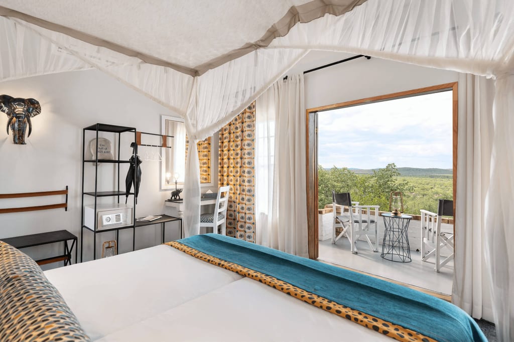 Lodge-Schlafzimmer mit Moskitonetz und Balkonblick auf grüne Landschaft am Tag