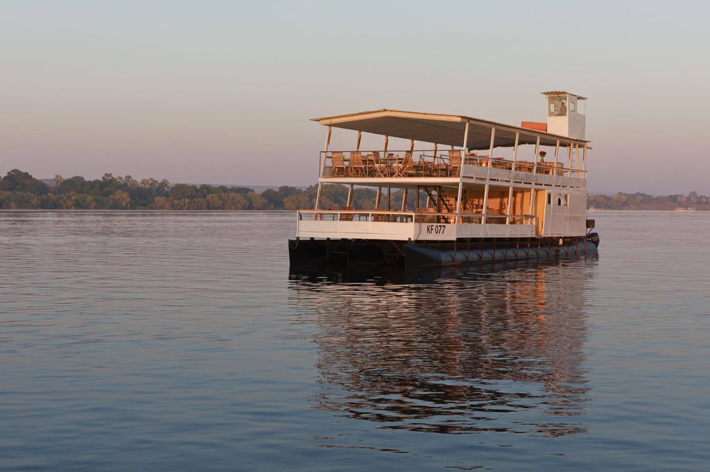Zweistöckiges Passagierboot auf ruhigem Gewässer im warmen Abendlicht, spiegelnde Wasseroberfläche.