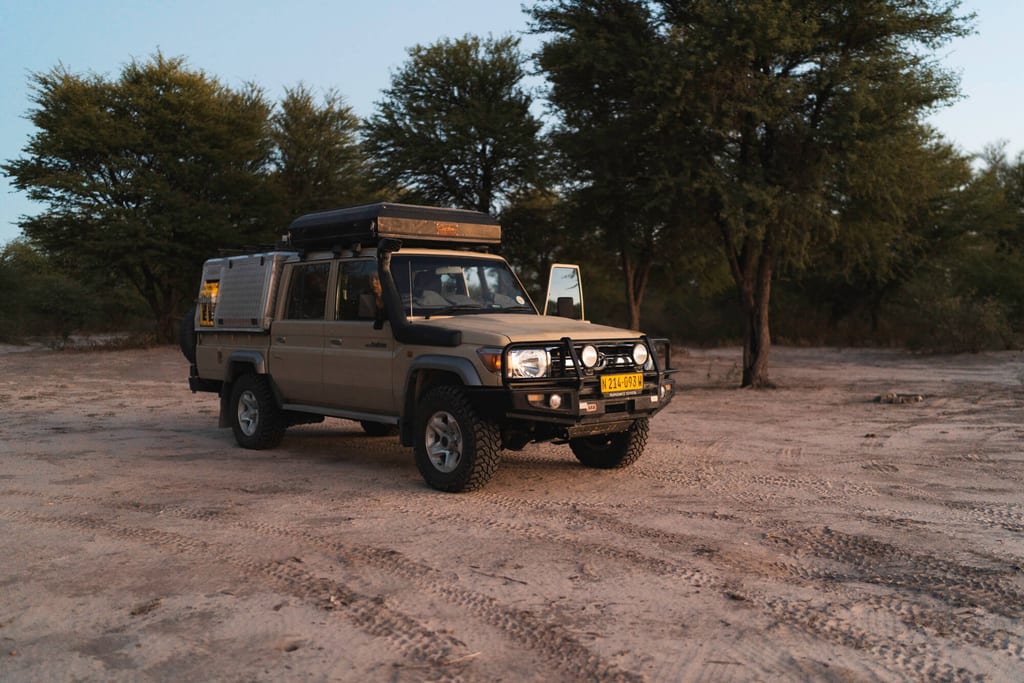 Expeditions-Geländewagen auf sandigem Boden bei Dämmerung vor baumbestandener Savanne