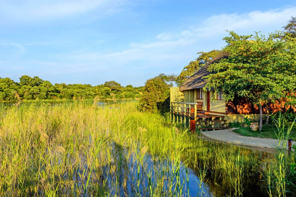 Strohgedeckte Lodge am Ufer mit hohem Schilf und ruhigem Wasser im warmen Abendlicht.