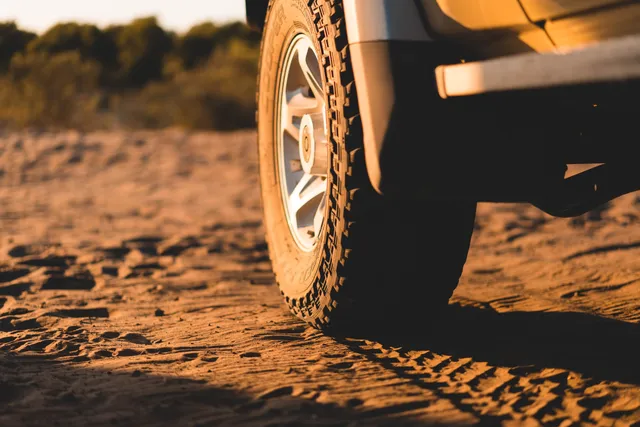 Nahaufnahme eines Offroad-Reifens im warmen Abendlicht auf sandigem Untergrund mit Reifenspuren