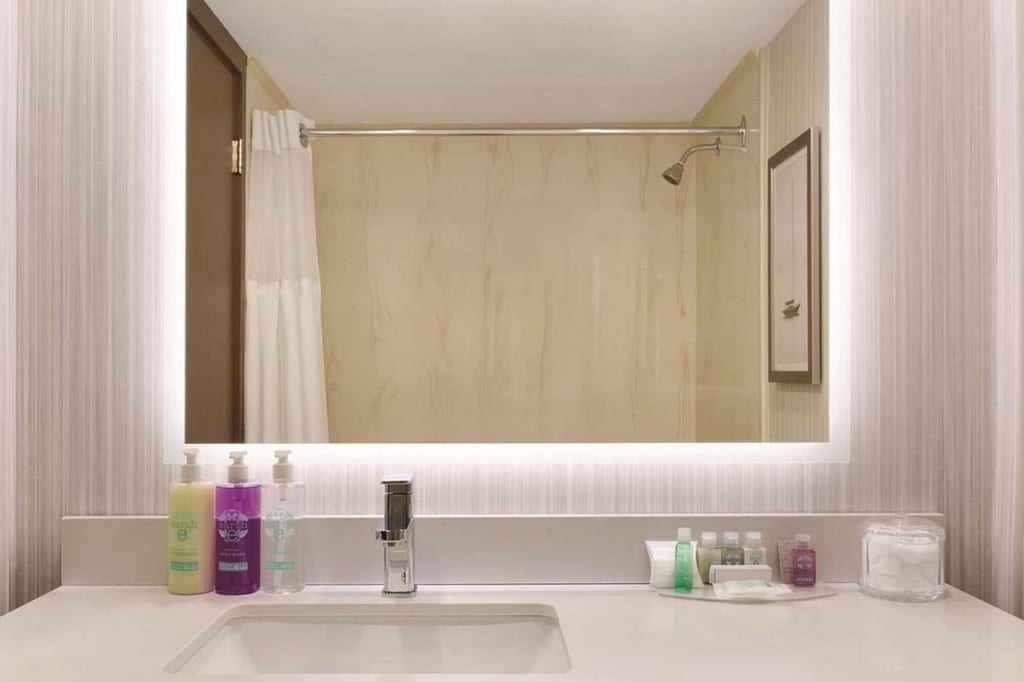 Modernes Hotelbadezimmer mit Waschbecken, beleuchtetem Spiegel und Toilettenartikeln auf der Arbeitsplatte.