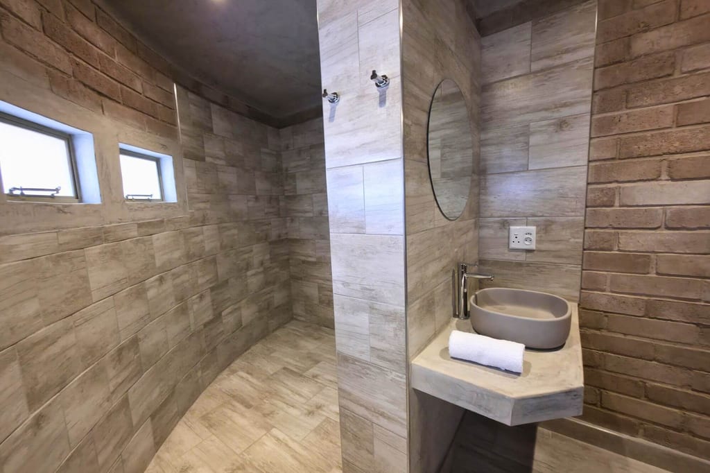 Modernes Badezimmer mit begehbarer Dusche, Waschtisch und Rundspiegel, neutral getöntes Licht