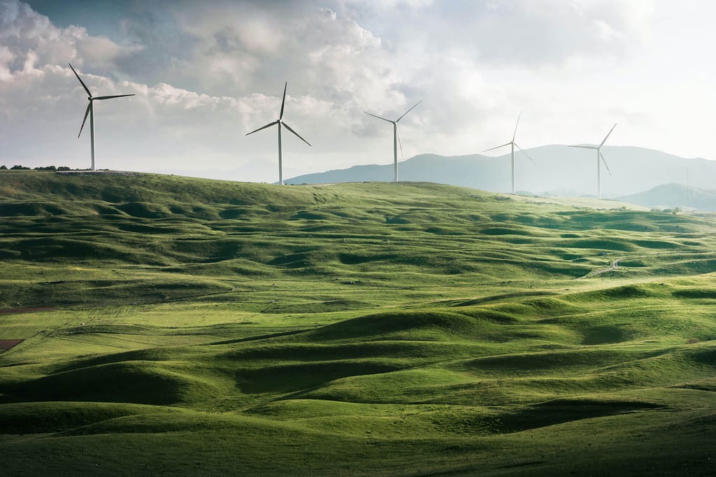 Panorama grüner, gewellter Hügel mit fünf Windkraftanlagen und bewölktem Himmel