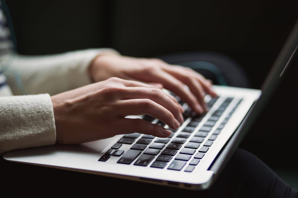 Nahaufnahme von Händen, die auf der Laptop-Tastatur tippen, seitliches weiches Licht.