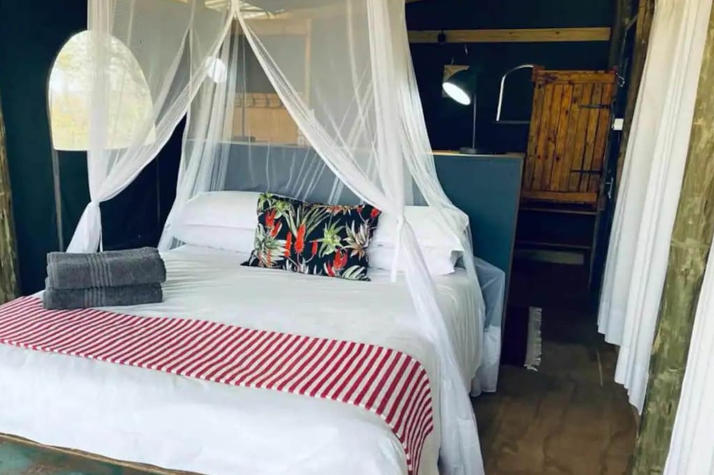 Innenaufnahme eines gemütlichen Lodgebetts mit Moskitonetz, dekorativem Kissen und gefalteten Handtüchern